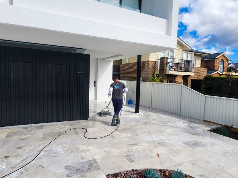 Worker high pressure cleaning a concrete driveway